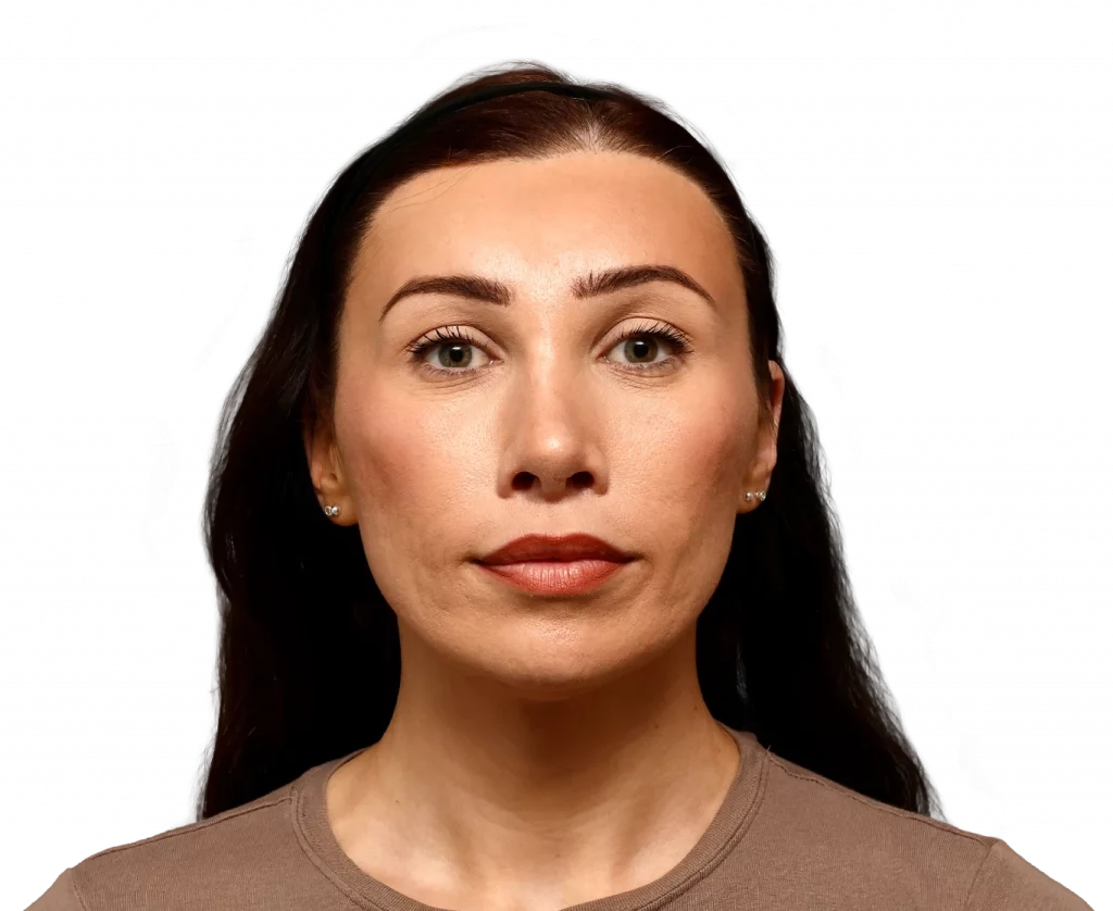 Portrait of a woman with long dark hair, wearing a brown shirt, looking straight ahead with a neutral expression against a black background.