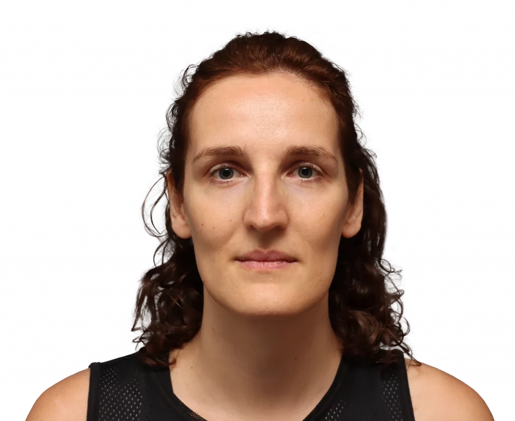 Front-facing head-and-shoulders portrait of a woman with brown, wavy hair wearing a black athletic top, neutral expression, against a black background.