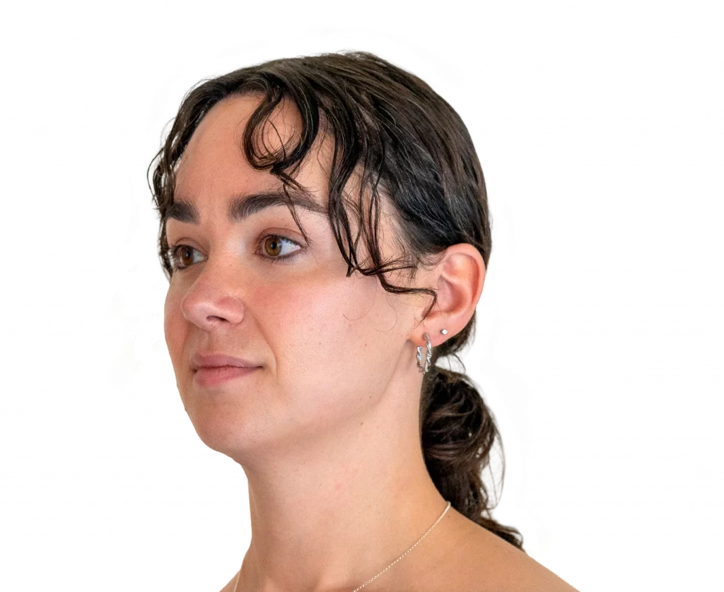 Portrait of a young woman with brown hair tied back, looking to the left, wearing small hoop earrings and a delicate necklace.
