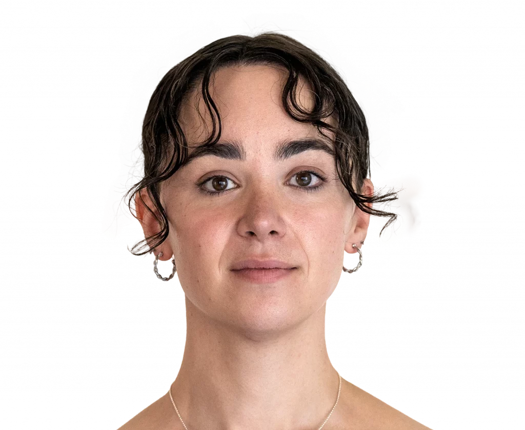 Close-up portrait of a woman with short dark wavy hair, brown eyes, hoop earrings, and a neutral expression facing the camera.