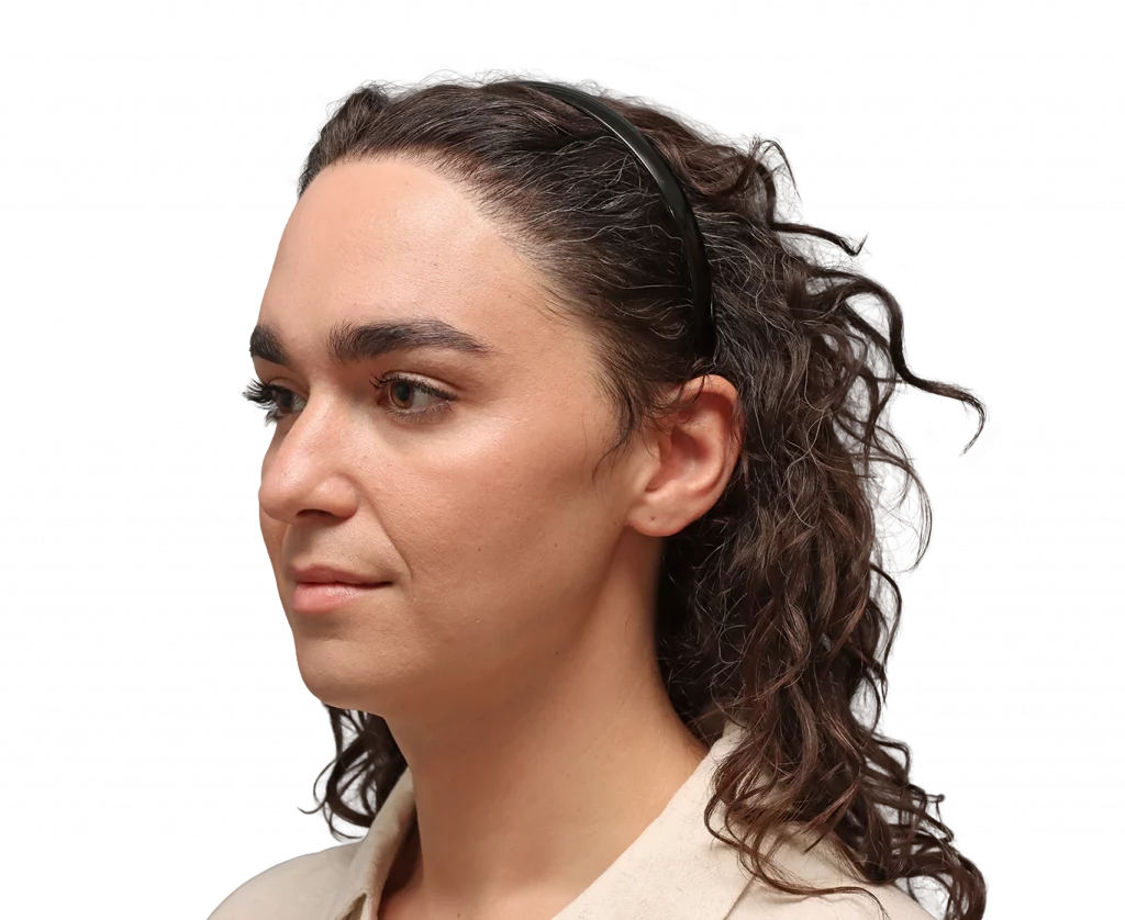 Profile view of a woman with dark curly hair held back by a black headband, wearing a beige shirt.
