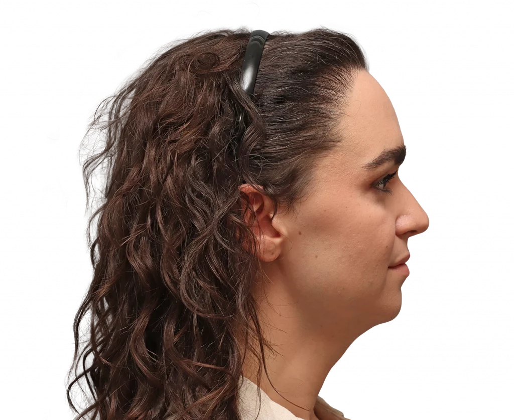 Side profile of a woman with dark, wavy hair pulled back and a small black hair clip visible at the crown.