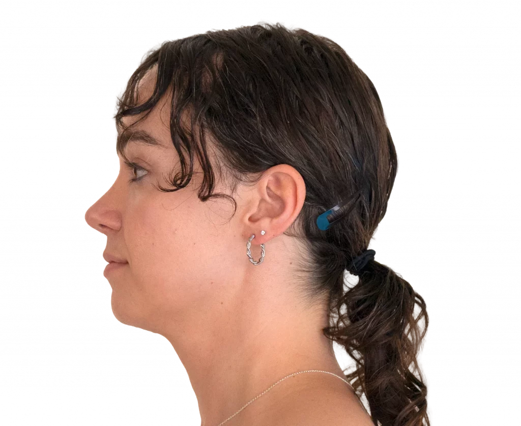 Profile view of a young woman with dark hair, wearing a blue hair clip and hoop earring near the ear.