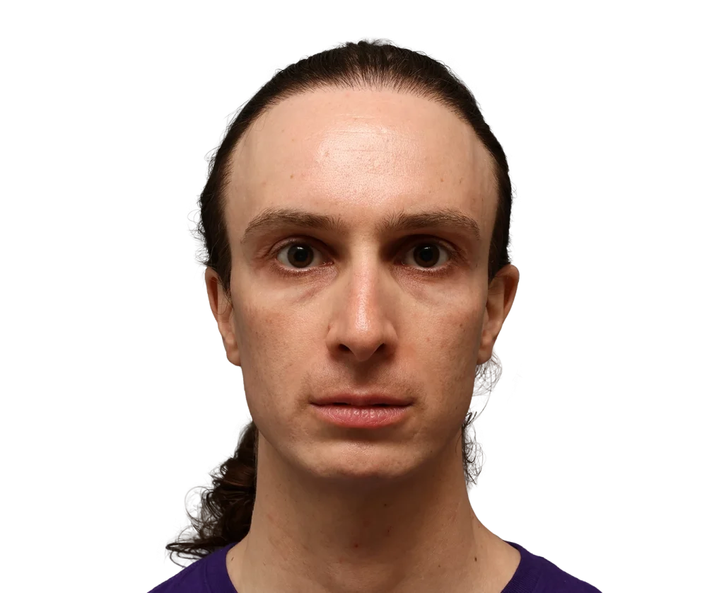 Close-up headshot of a person with brown hair tied back, wearing a purple shirt, neutral expression against a black background.