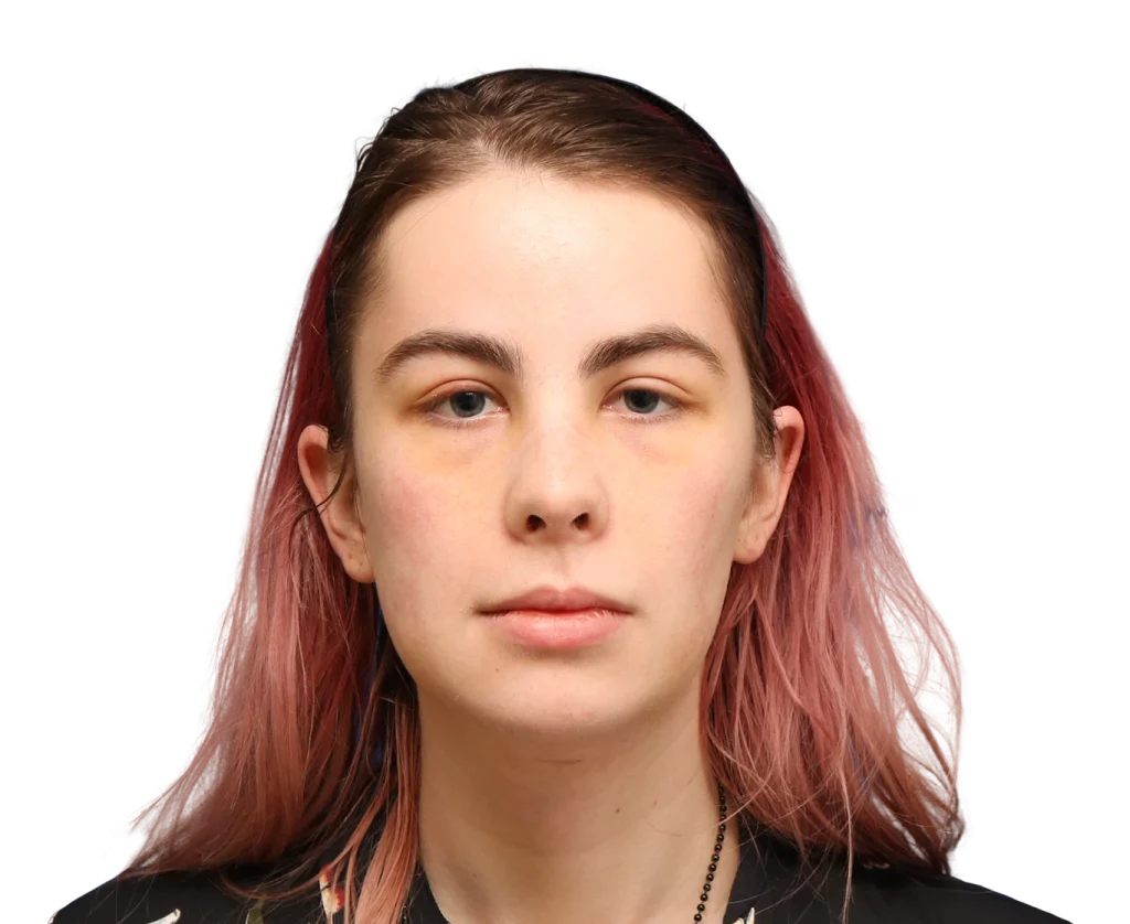 Close-up portrait of a person with pink hair, neutral expression, facing forward a.t the camera.