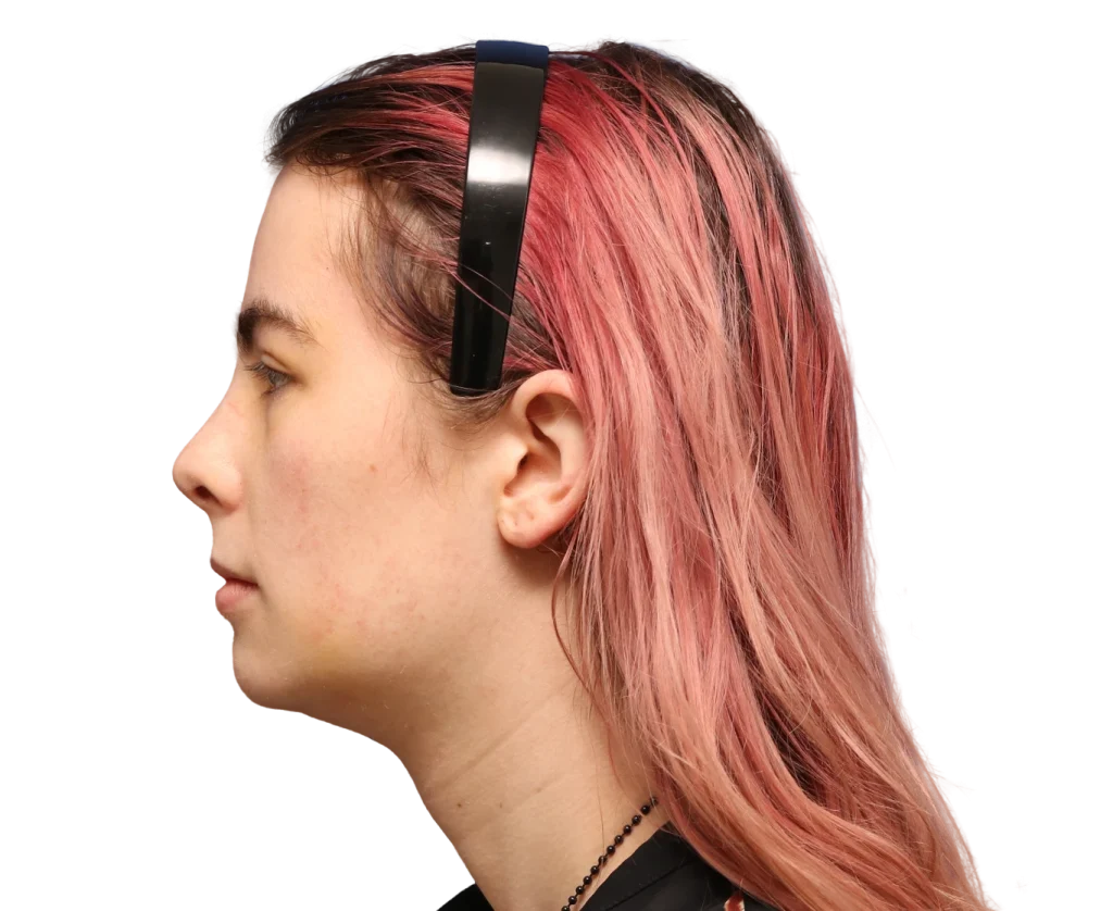 Profile of a person with pink-dyed hair wearing black over-ear headphones, facing left