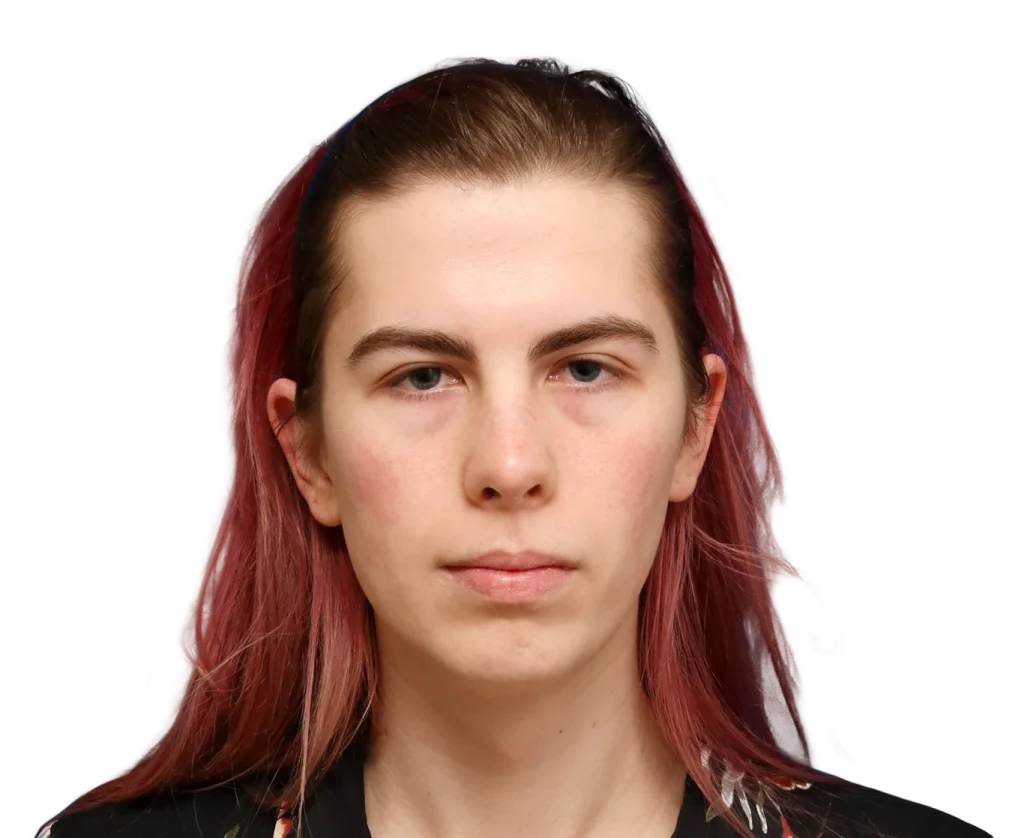 Close-up headshot of a young person with pinkish-red hair and neutral expression against a black background.