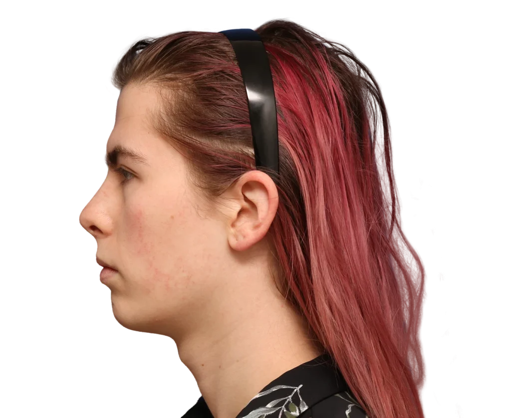 Profile view of a person with pink-dyed hair wearing a black headband, facing left.