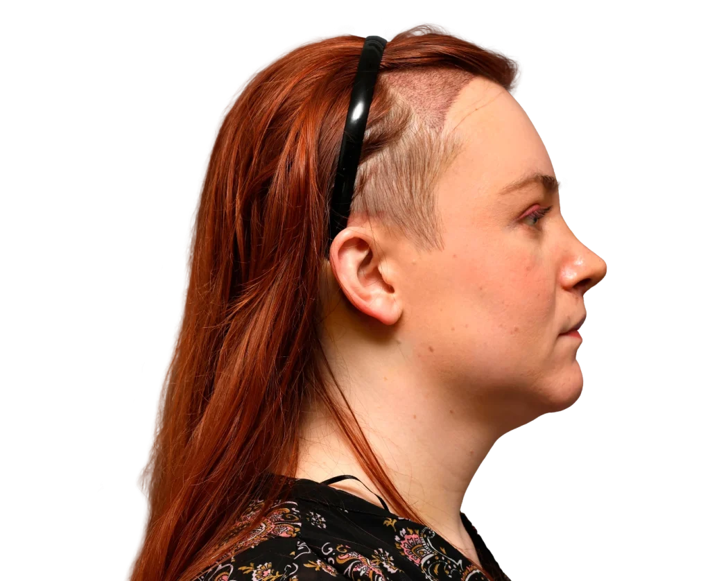 Side profile of a woman with red hair and a shaved undercut, wearing a black headband against a black background.