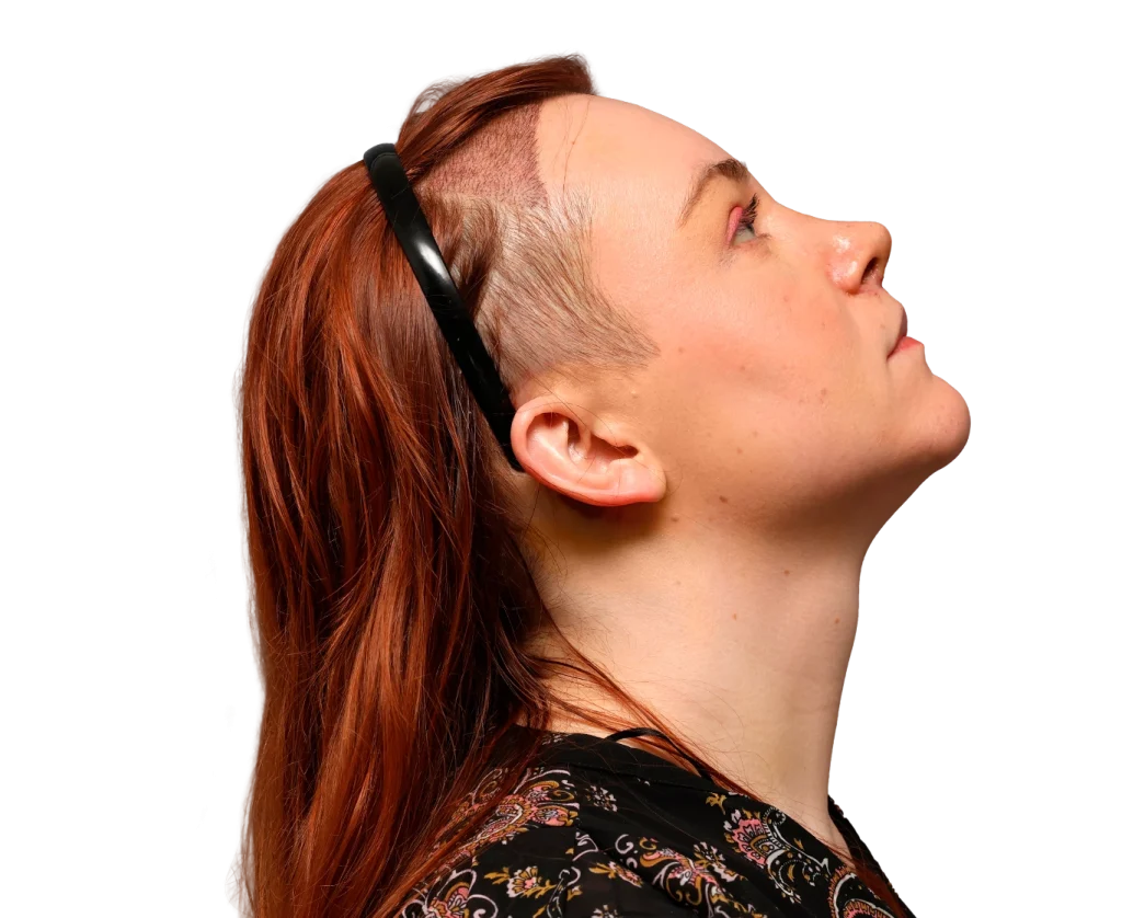 Side profile of a woman with red hair wearing a black headband, looking up to the right.