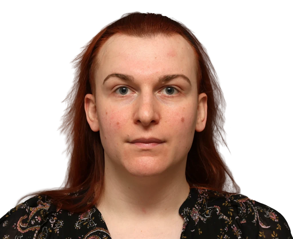 Head-and-shoulders portrait of a woman with red hair, facing the camera with a neutral expression, wearing a patterned blouse