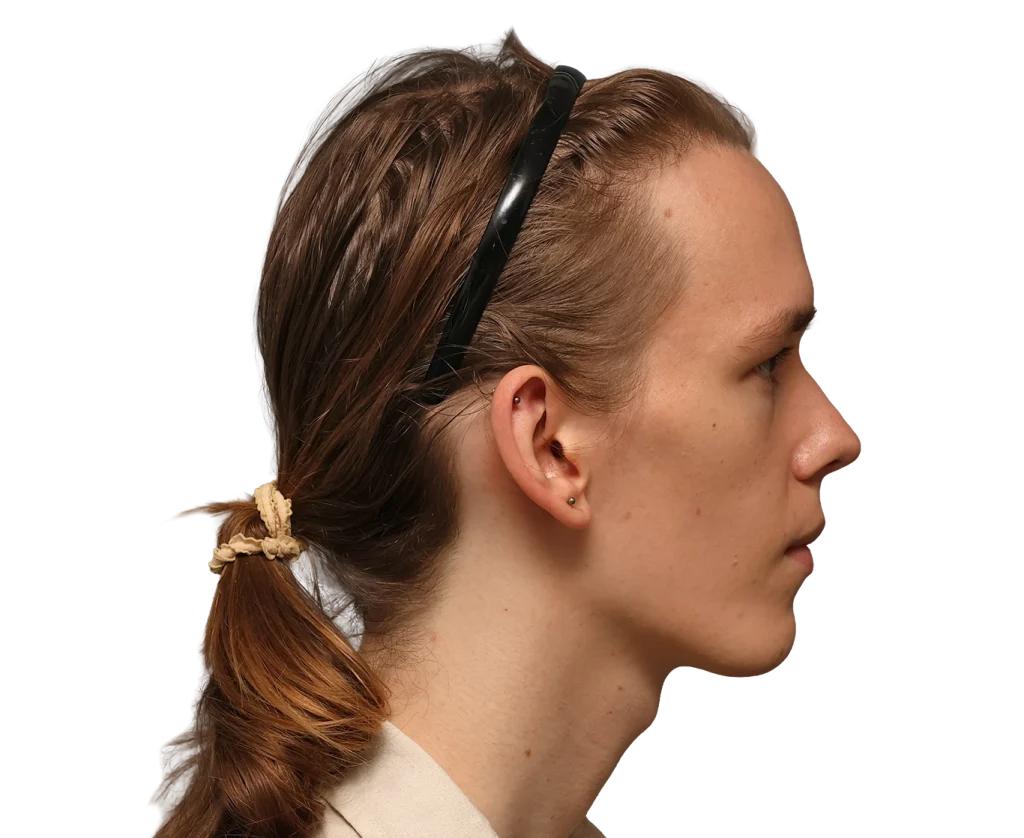 Side profile of a young woman with brown hair tied in a low ponytail, sunglasses resting on her head.